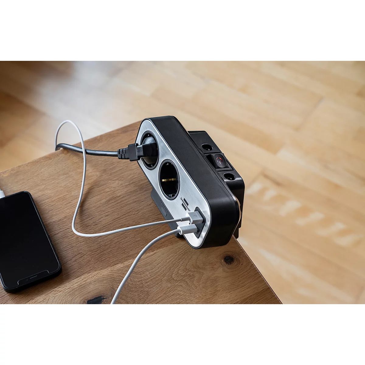 Zwart stekkerblok met USB-poorten, een smartphone en kabels op een houten oppervlak.