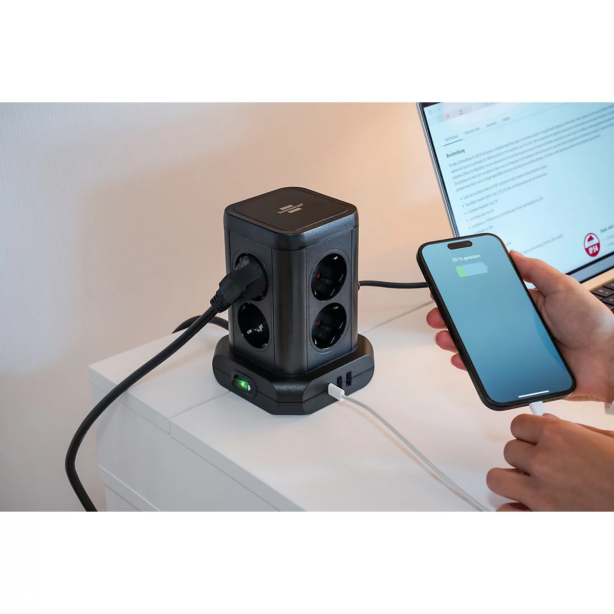 Multiprise noire rechargeant smartphone et ordinateur portable. Une main branche un câble de chargement sur le téléphone.