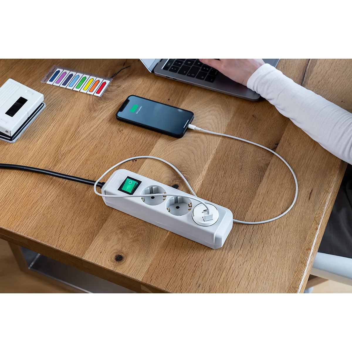 Close-up: Een hand opent een klep van een zwarte stekkerdoos met USB-poorten. De achtergrond is houtnerf.