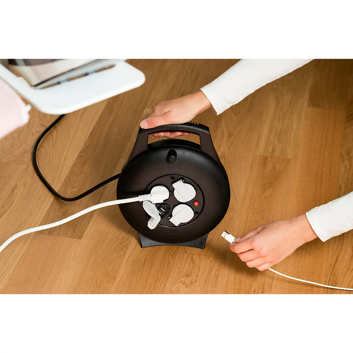 Gros plan d'une multiprise ronde noire avec des couvercles de prise blancs et une LED rouge. Un câble blanc est branché.