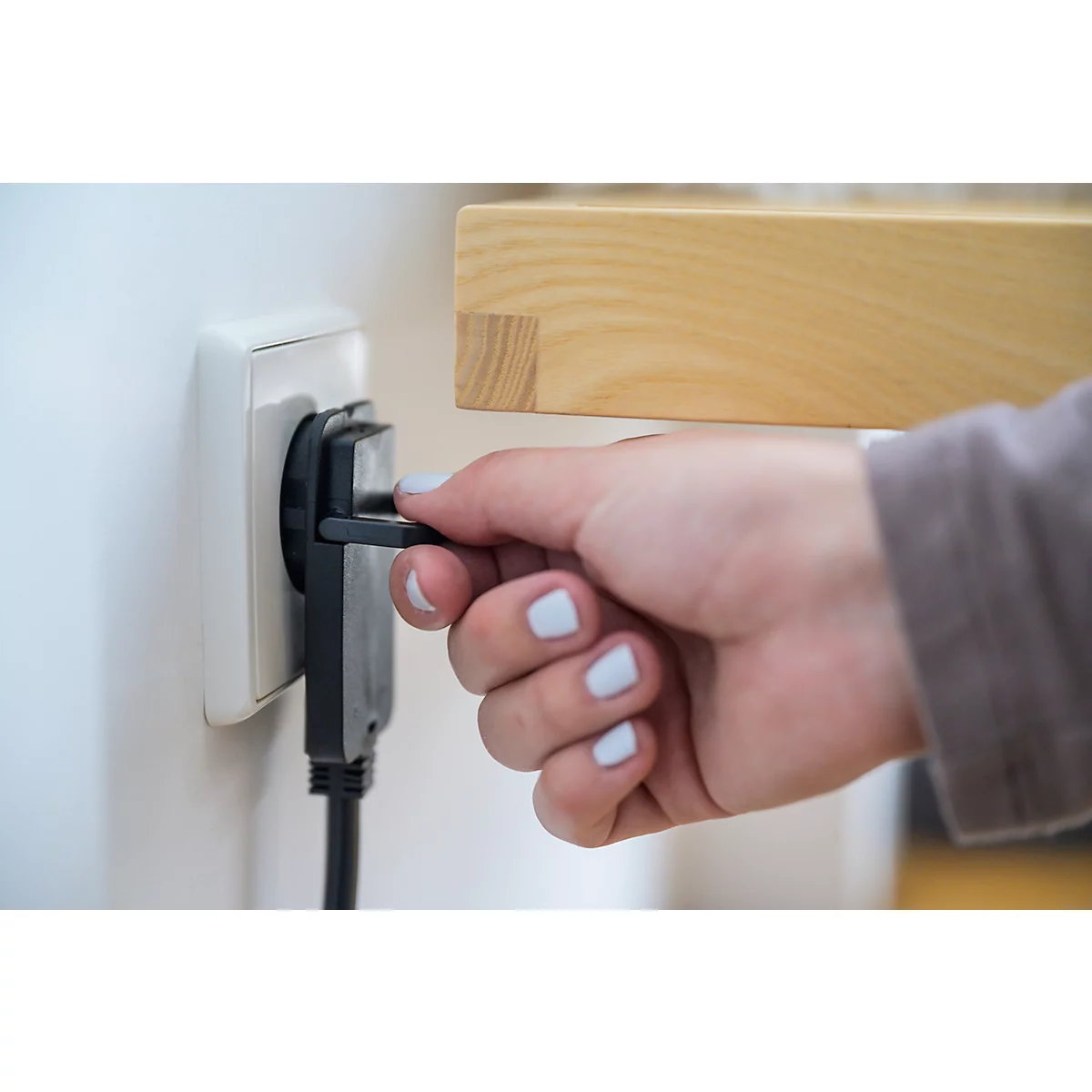 Eine Hand steckt einen schwarzen Stecker in eine weiße Steckdose.