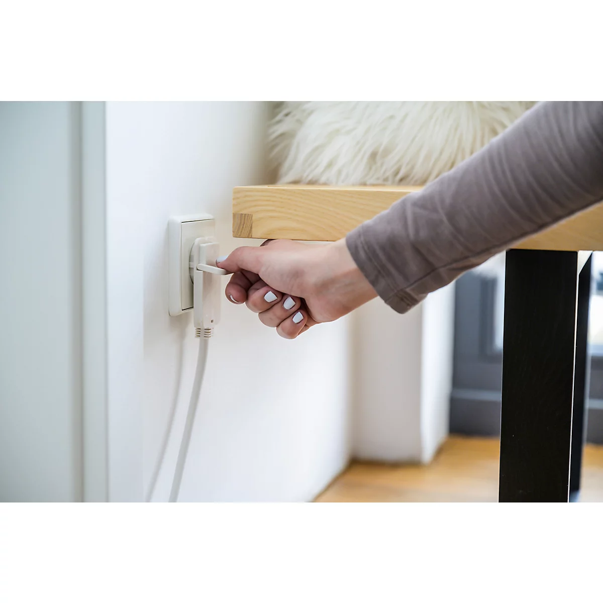 Wit stopcontact met witte stekker en kabel aan een gestructureerde muur.