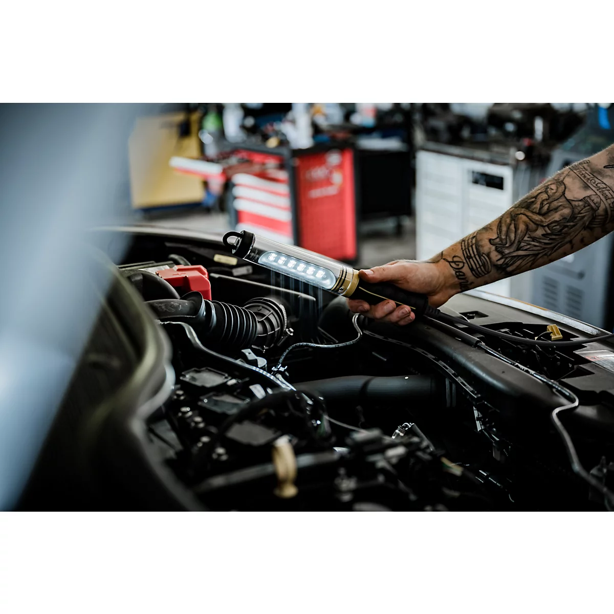 Monteur verlicht een motorcompartiment met een LED-lamp. De arm is getatoeëerd.