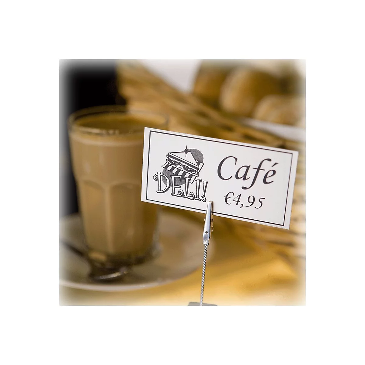 Ein Glas Kaffee, neben einem Schild mit "Café" und Preis. Im Hintergrund Körbe mit Backwaren.