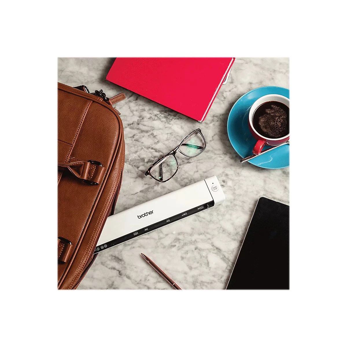 Draufsicht: braune Tasche, Brille, rotes Notizbuch, Kaffee, Scanner und Tablet auf marmoriertem Tisch.