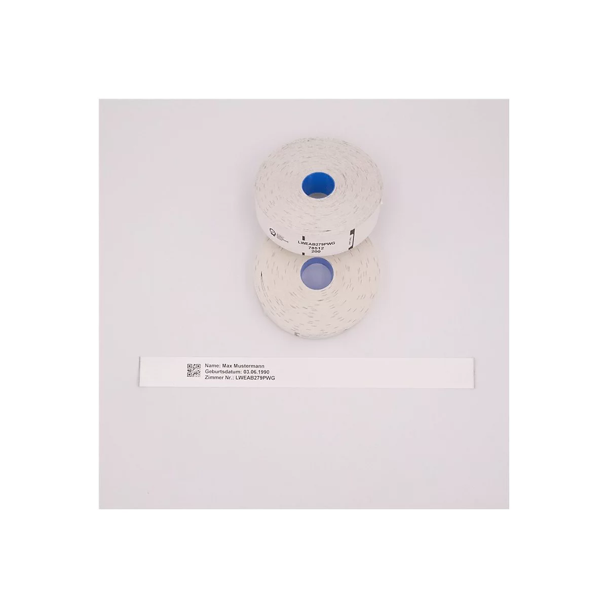 Zwei Rollen weißes Etikettenpapier mit blauem Kern liegen übereinander. Darunter ein Etikett mit Text und QR-Code.
