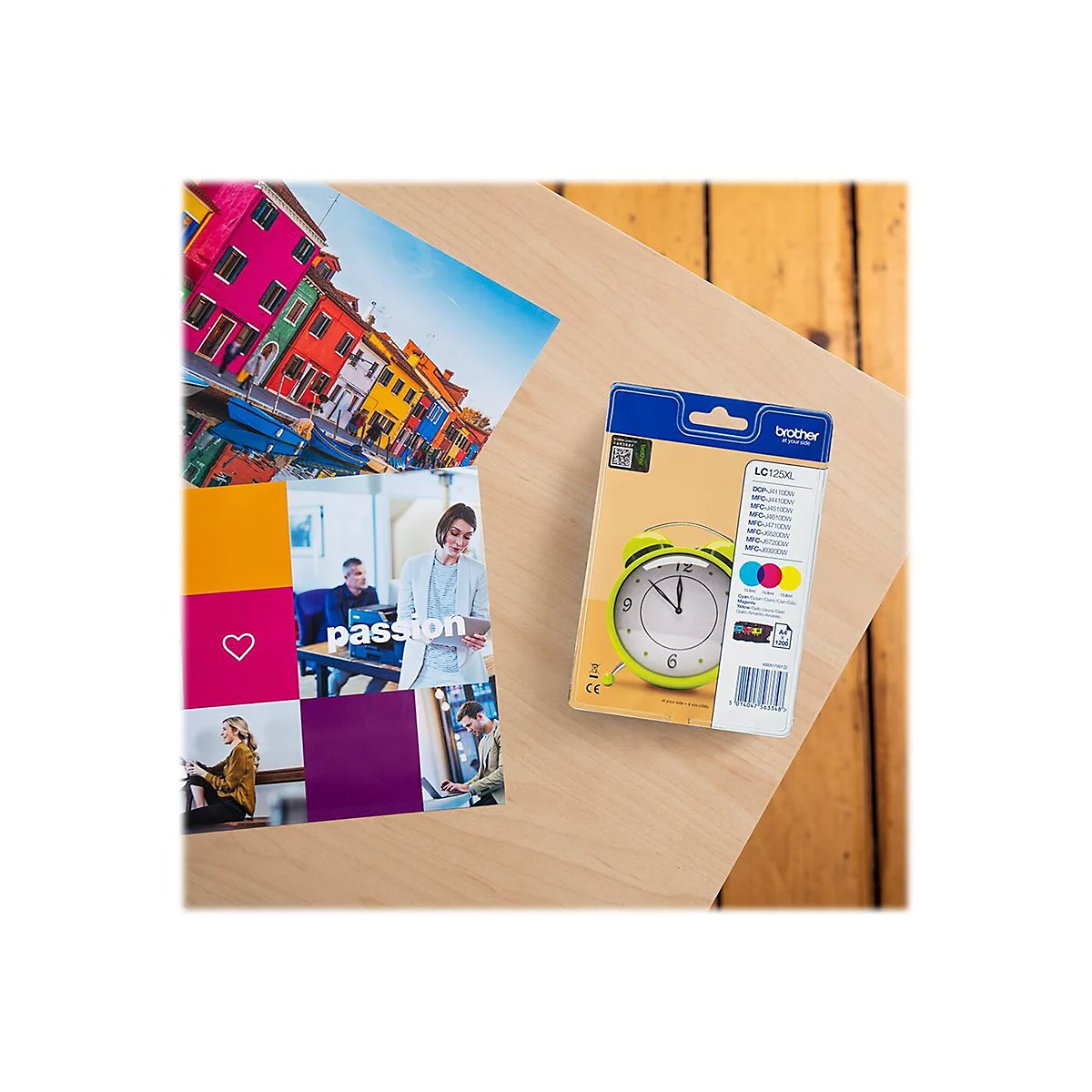 Druckerpatronen-Verpackung von Brother, neben einem Magazin mit farbenfrohen Fotos und einem gelben Wecker.