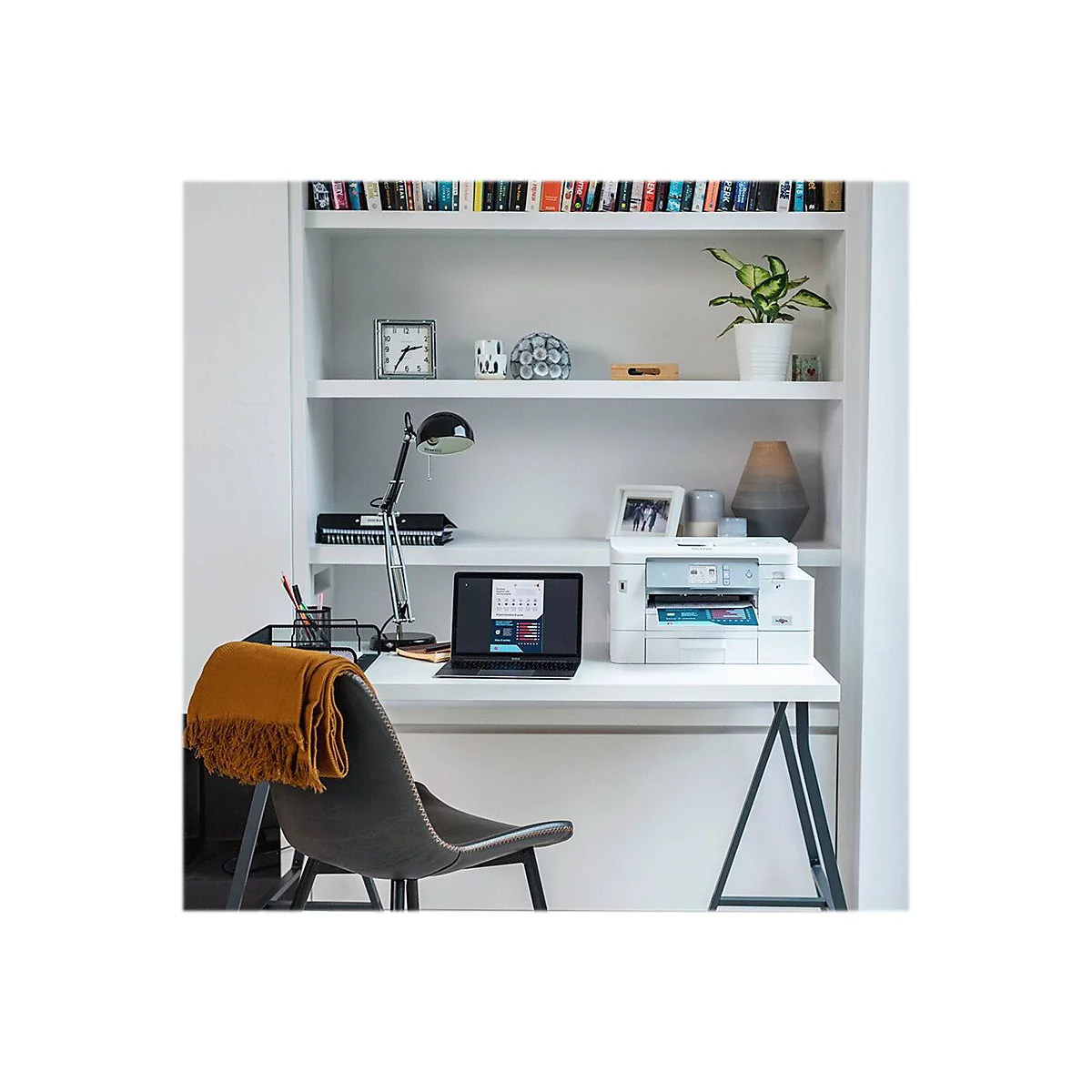Ein moderner Arbeitsplatz: Schreibtisch mit Drucker, Laptop und Lampe, Bücherregal im Hintergrund.