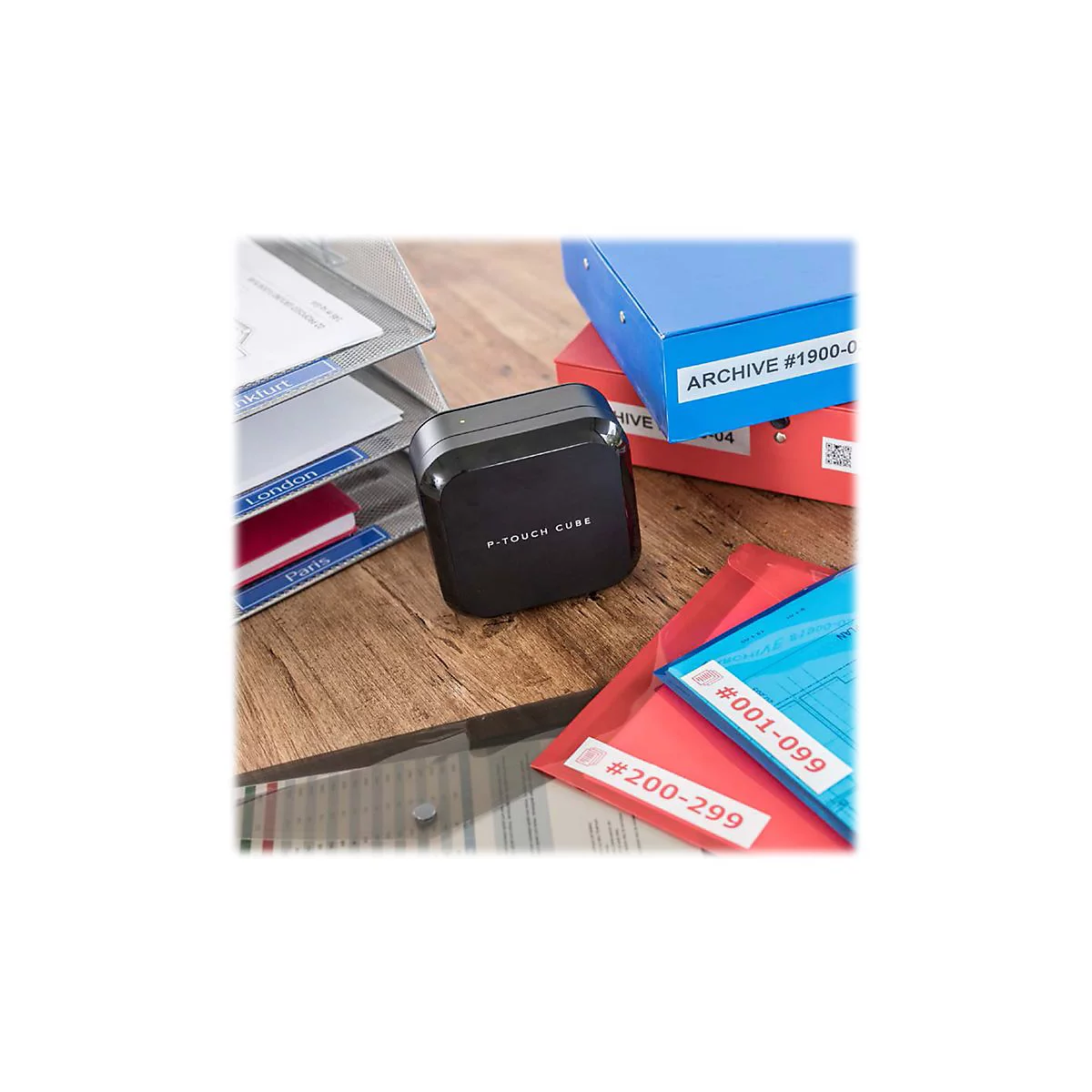 Ein schwarzes P-Touch Cube BeschriftungsgerÃ¤t neben beschrifteten Ordnern und Mappen auf einem Holztisch.