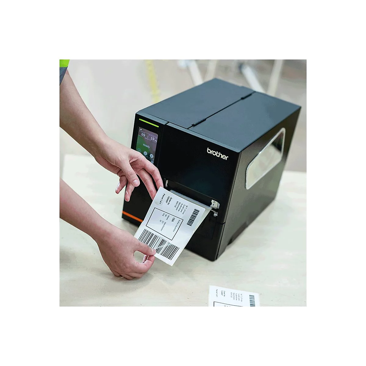 Person zieht ein Etikett aus einem schwarzen Brother Etikettendrucker. Das Etikett zeigt Barcodes und Text.