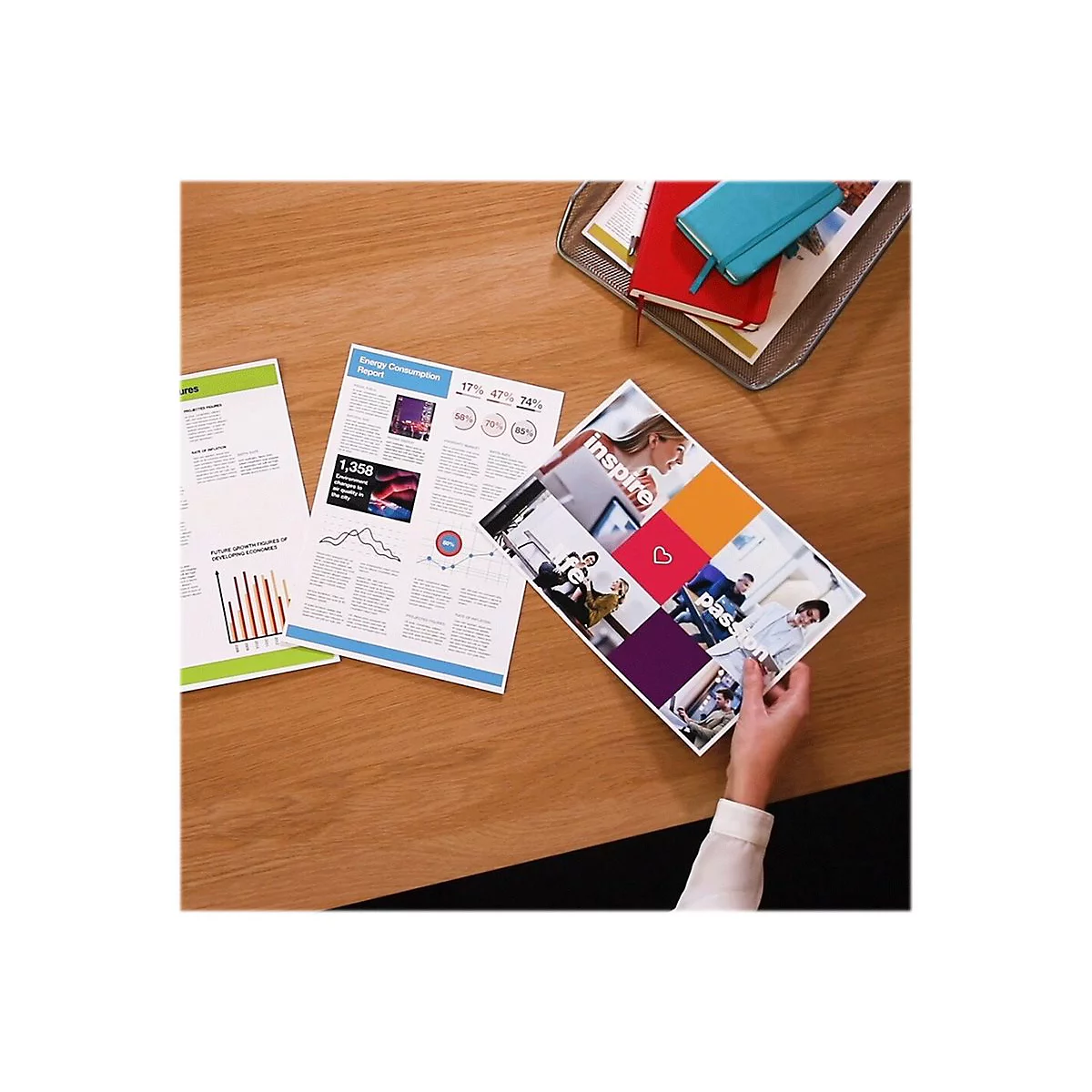 Auf einem Holztisch liegen Dokumente: Diagramme, Tabellen und ein Magazin mit dem Wort "inspire". Eine Hand hält das Magazin.