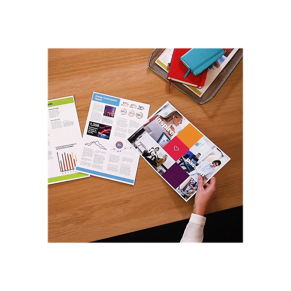 Nahaufnahme von Dokumenten und Notizbüchern auf einem Holztisch. Eine Hand hält ein Magazin mit dem Wort "inspire".