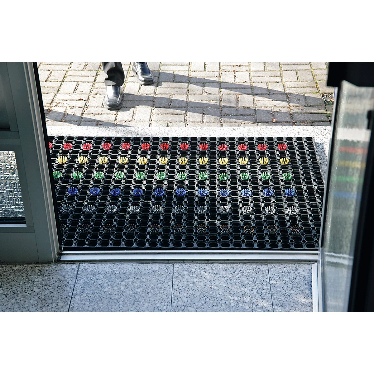 Black doormat with colorful hands. Person in shoes entering room through door.