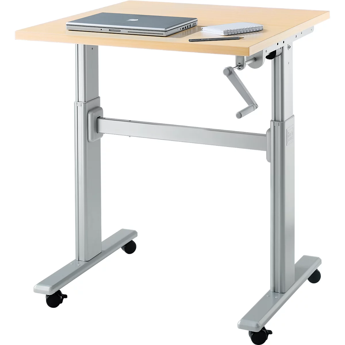 Bureau réglable en hauteur avec ordinateur portable et bloc-notes. Plateau de table brun clair, cadre argenté, roulettes noires. Manivelle pour le réglage en hauteur.