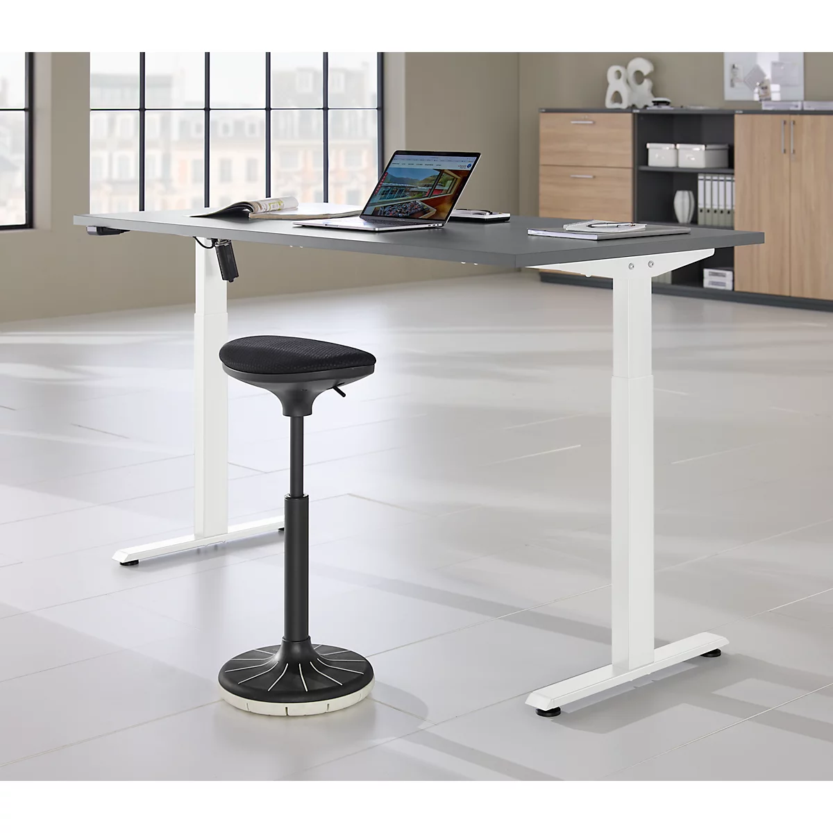 Lichtgrijze statafel met zwarte kruk, laptop, documenten. Ramen en kasten op de achtergrond.