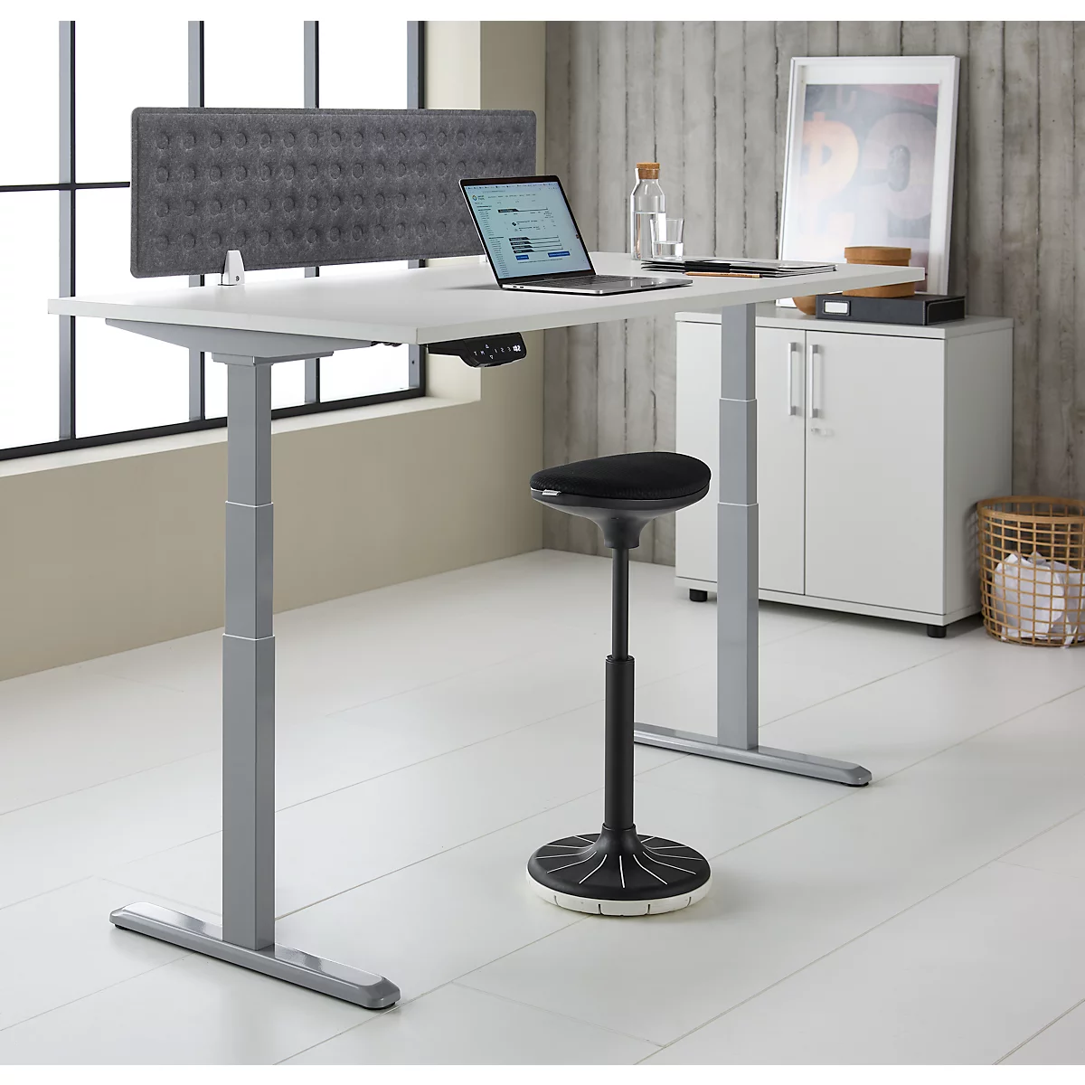 Een in hoogte verstelbaar bureau met laptop, stoel, grijze gewatteerde muur en accessoires. Heldere, moderne kantooropstelling.