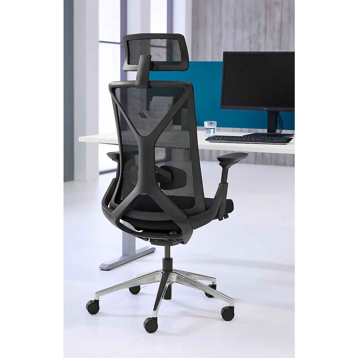 Zwarte bureaustoel met mesh rug. Hij staat voor een bureau met een computer.