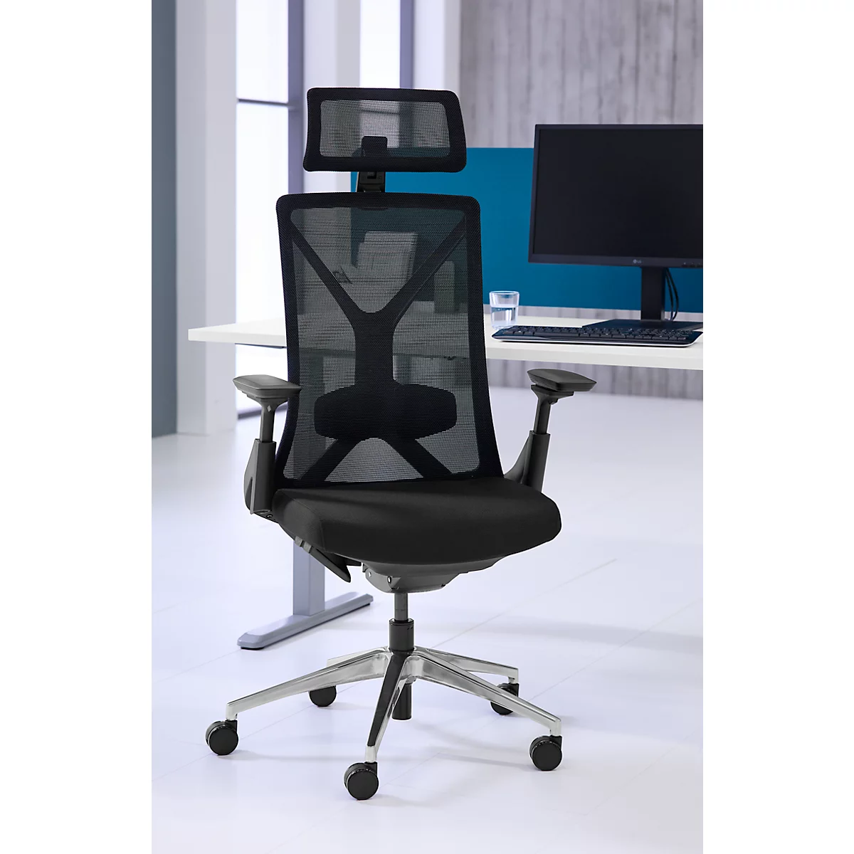 Zwarte bureaustoel met mesh rug en hoofdsteun voor een bureau met computer.