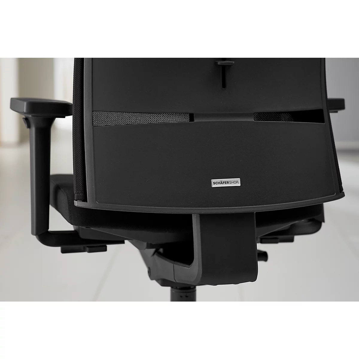 Close-up van een zwarte bureaustoel met de rugleuning en armleuning. Klein bordje met opschrift.