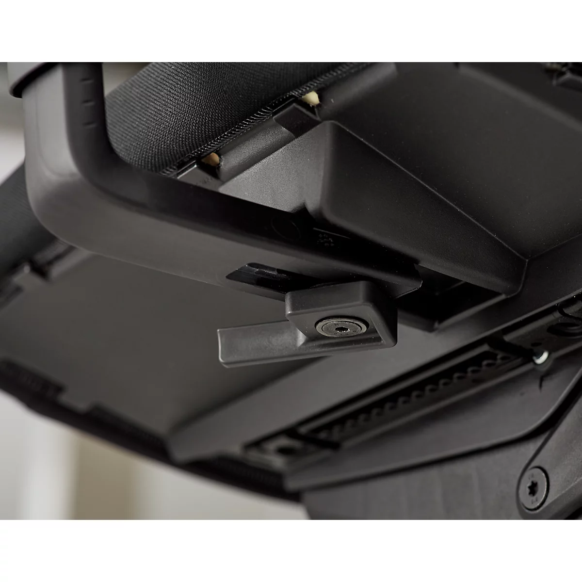 Detail van een zwarte metalen sluiting met hendel en schroef. Een deel van de rugleuning is zichtbaar.