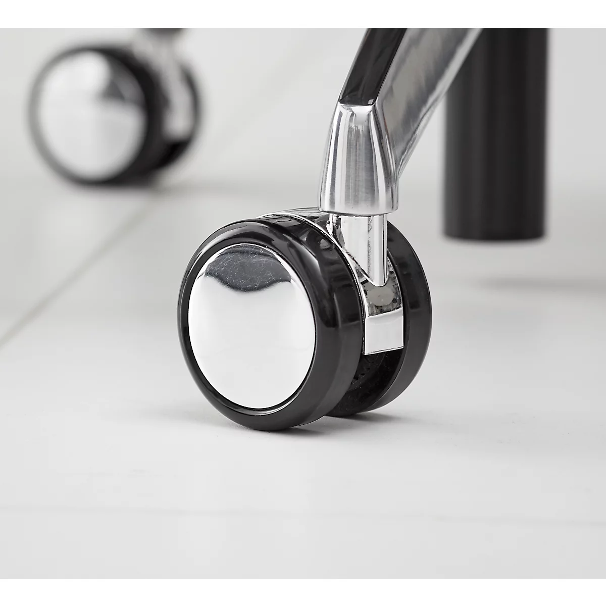 Close-up van twee stoelwielen, chromekleur, zwarte band, op een lichte vloer.