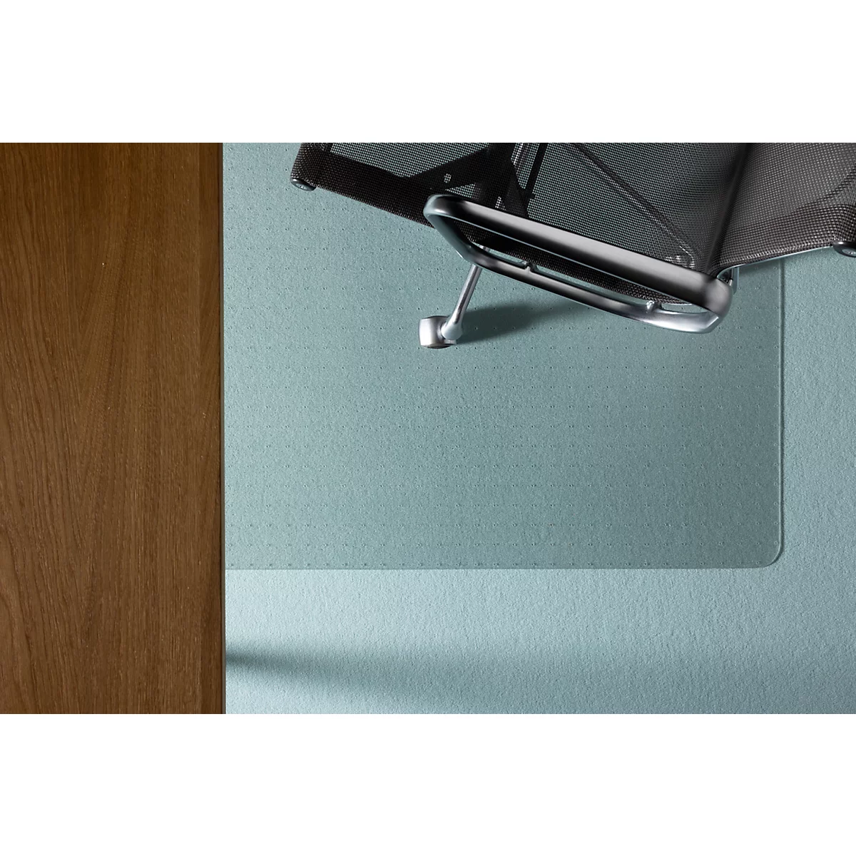 Bovenaanzicht van een bureaustoel en een bureaumat. Het been van de stoel staat op de mat. Een houten tafel staat links.