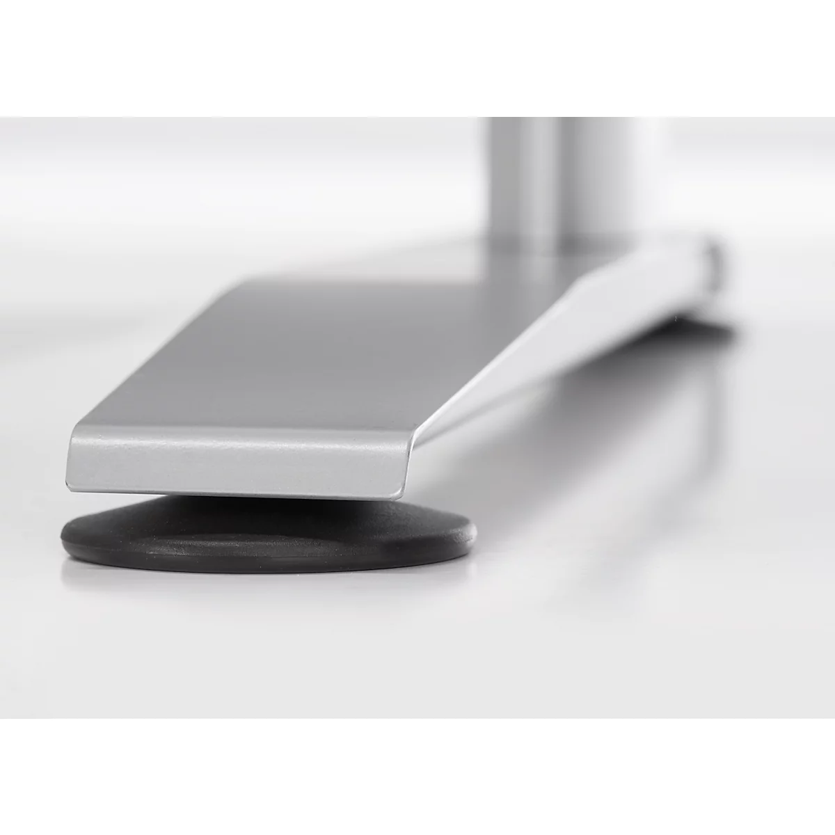 Close-up van een zilveren metalen voet op een zwarte rubberen buffer, staand op een wit oppervlak.