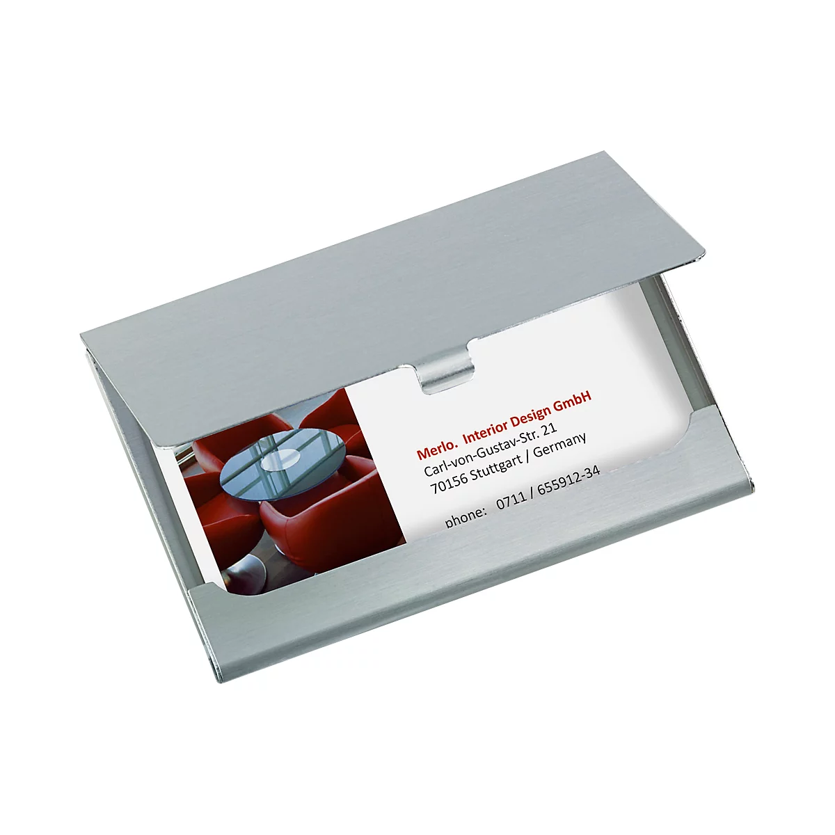 Silver business card holder displaying a business card with the Merlo. Interior Design GmbH logo. In the background, red armchairs are visible.