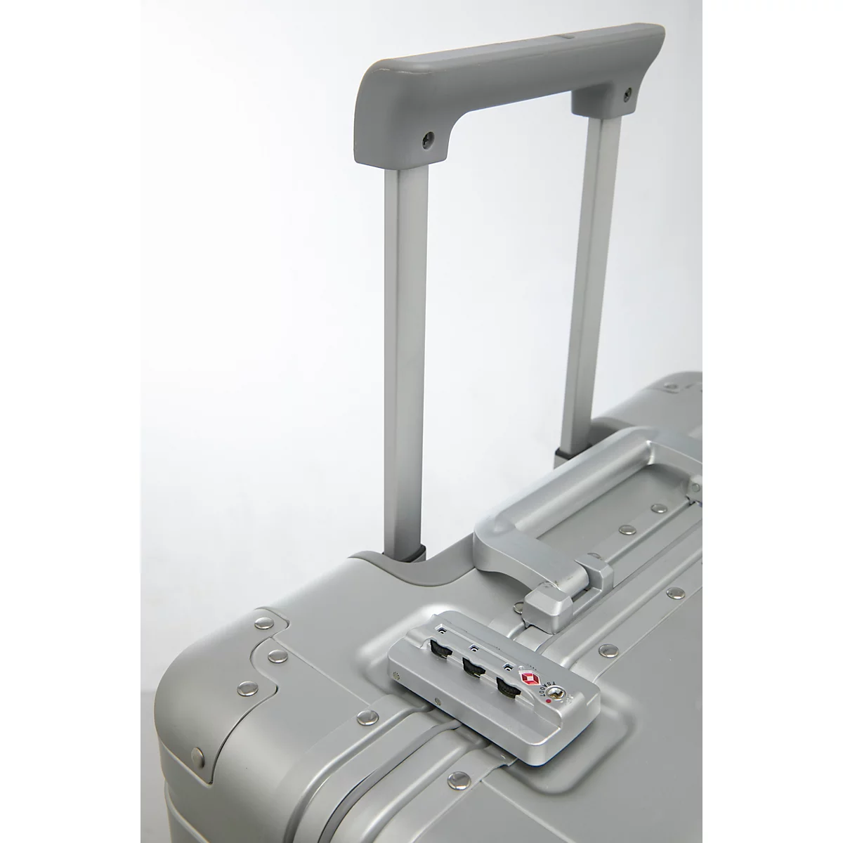 Gros plan sur une valise argentée avec poignée extensible, cadenas à combinaison et certification TSA.