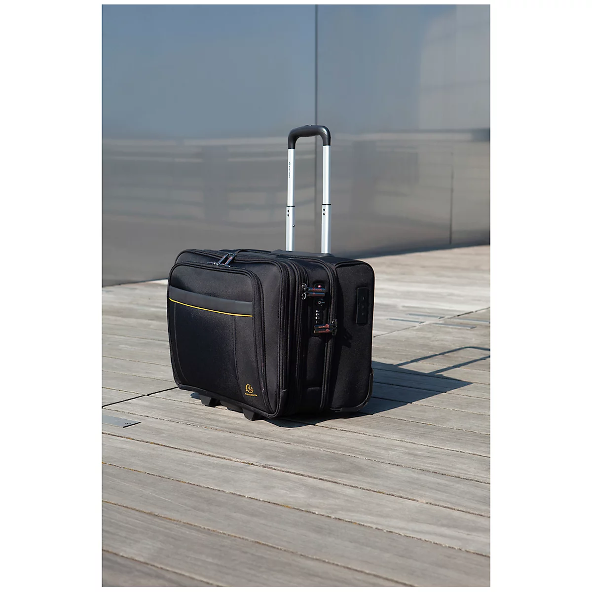 Black rolling suitcase with extendable handle standing on wooden planks against a gray background.