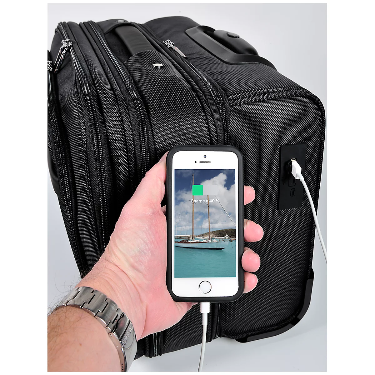 Black suitcase with a charging cable attached to a mobile phone. A sailboat is on the display. The suitcase is charging.