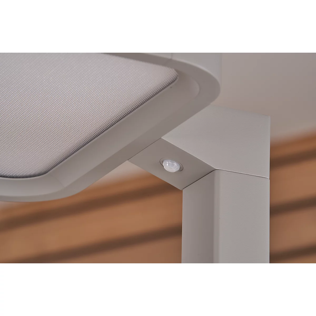 Close-up of a corner with a sensor. An angular pillar meets a rounded corner. In the corner is a small, round sensor. A shaded fabric is to the left.