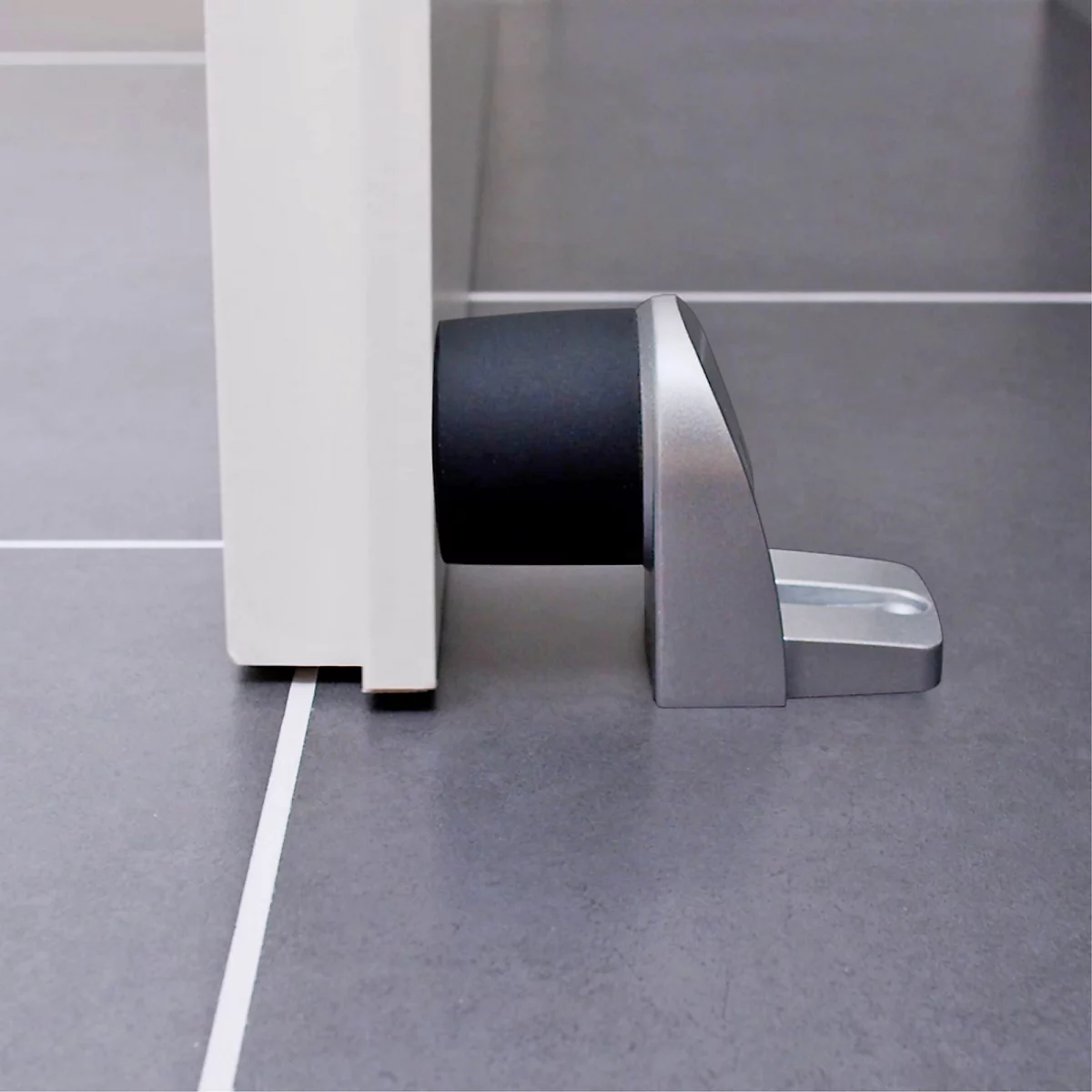 Gros plan d'une butée de porte. La butée est argentée et maintient une porte blanche.