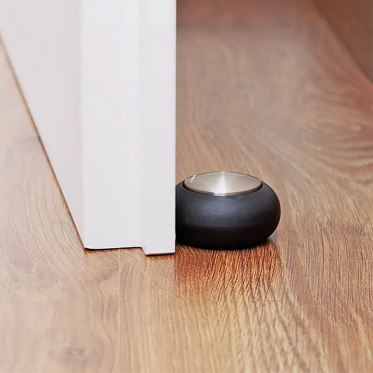 Un butoir de porte en caoutchouc noir maintenant une porte blanche ouverte sur un plancher en bois.