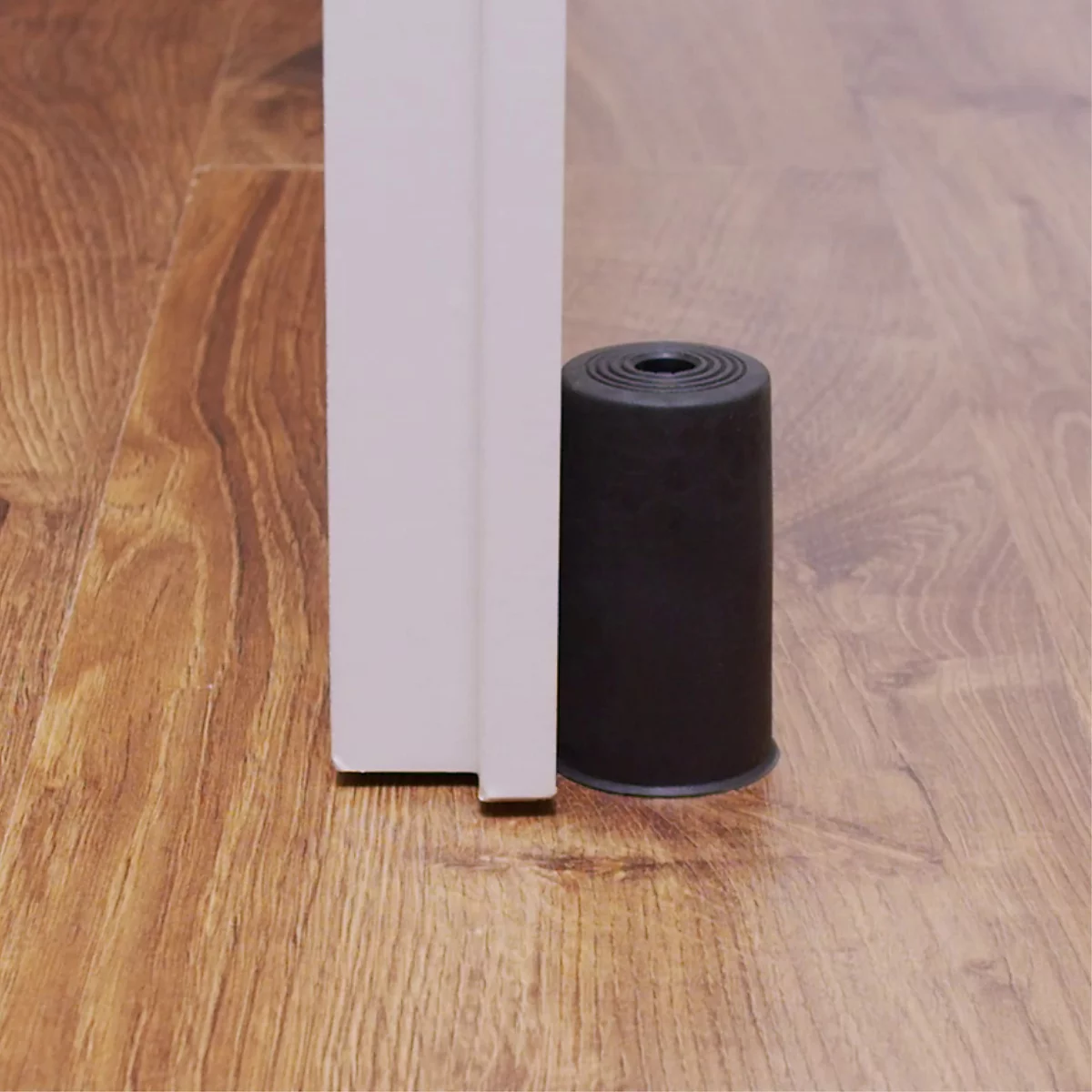 Butoir de porte noir au sol. Il empêche la porte de se fermer. Plancher en bois.