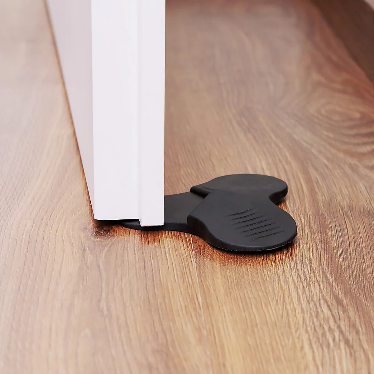 Butée de porte en caoutchouc noir sous une porte blanche sur un plancher en bois.