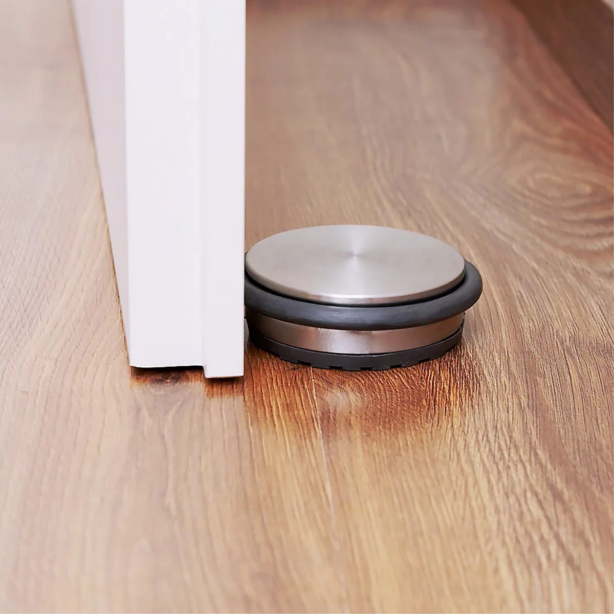 Un butoir de porte en métal et en caoutchouc maintient une porte ouverte sur un plancher en bois.