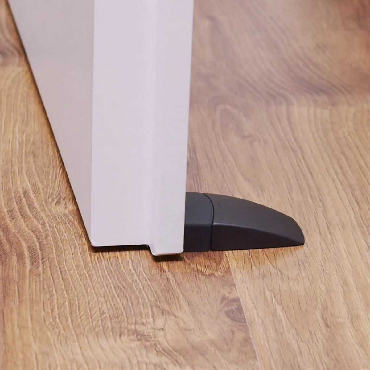 Un butoir de porte noir maintient une porte blanche, plancher en bois.