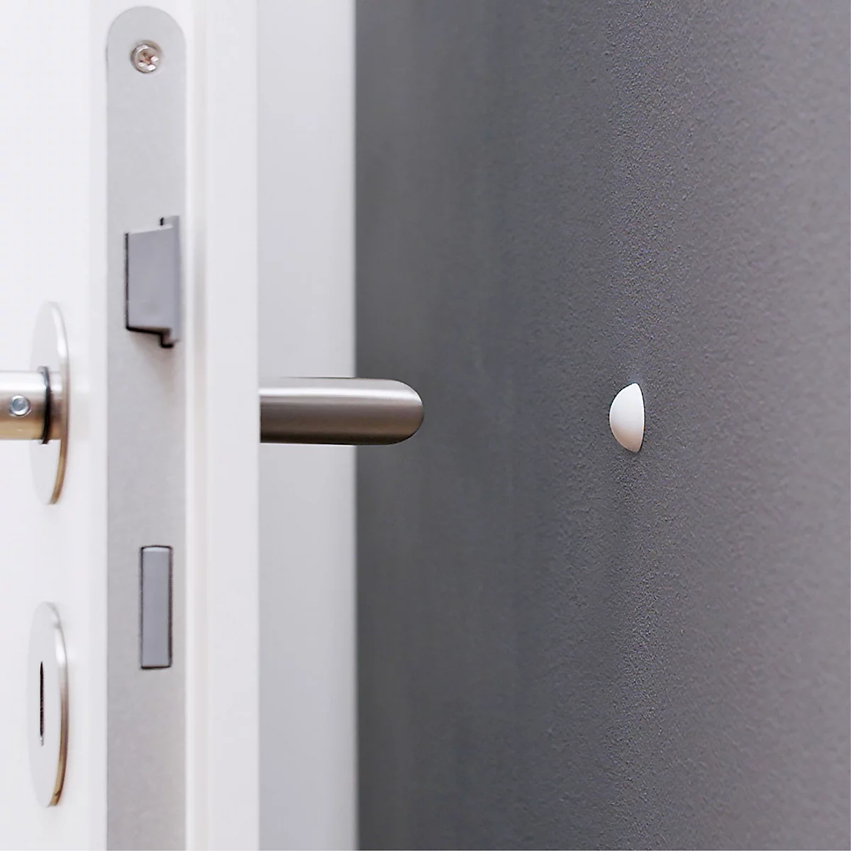 Gros plan d'une porte blanche avec poignée en acier inoxydable et un objet blanc, semi-circulaire sur le mur.