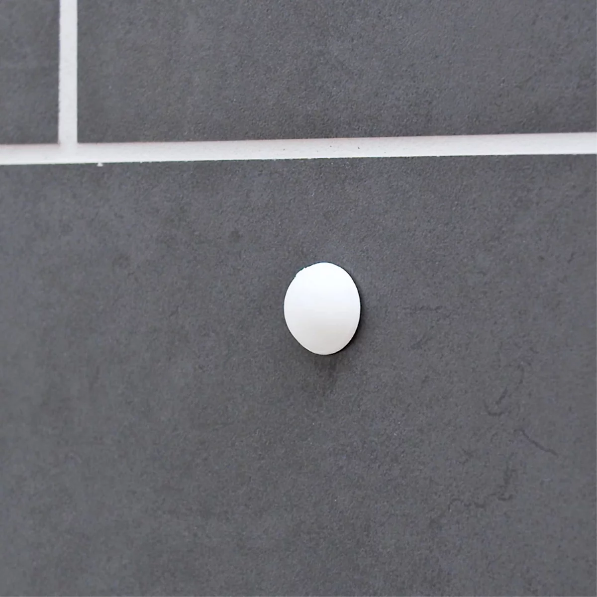 Un bouton blanc et rond sur un mur gris, avec des lignes blanches comme motif.