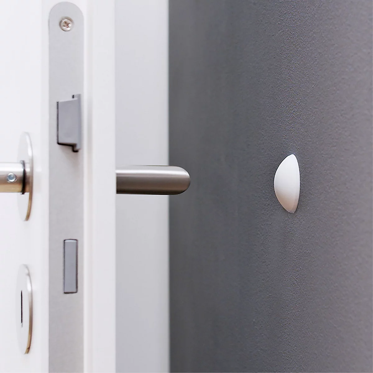 Gros plan d'une porte avec une poignée en métal, un cadre de porte blanc et un élément blanc semi-circulaire sur le mur.