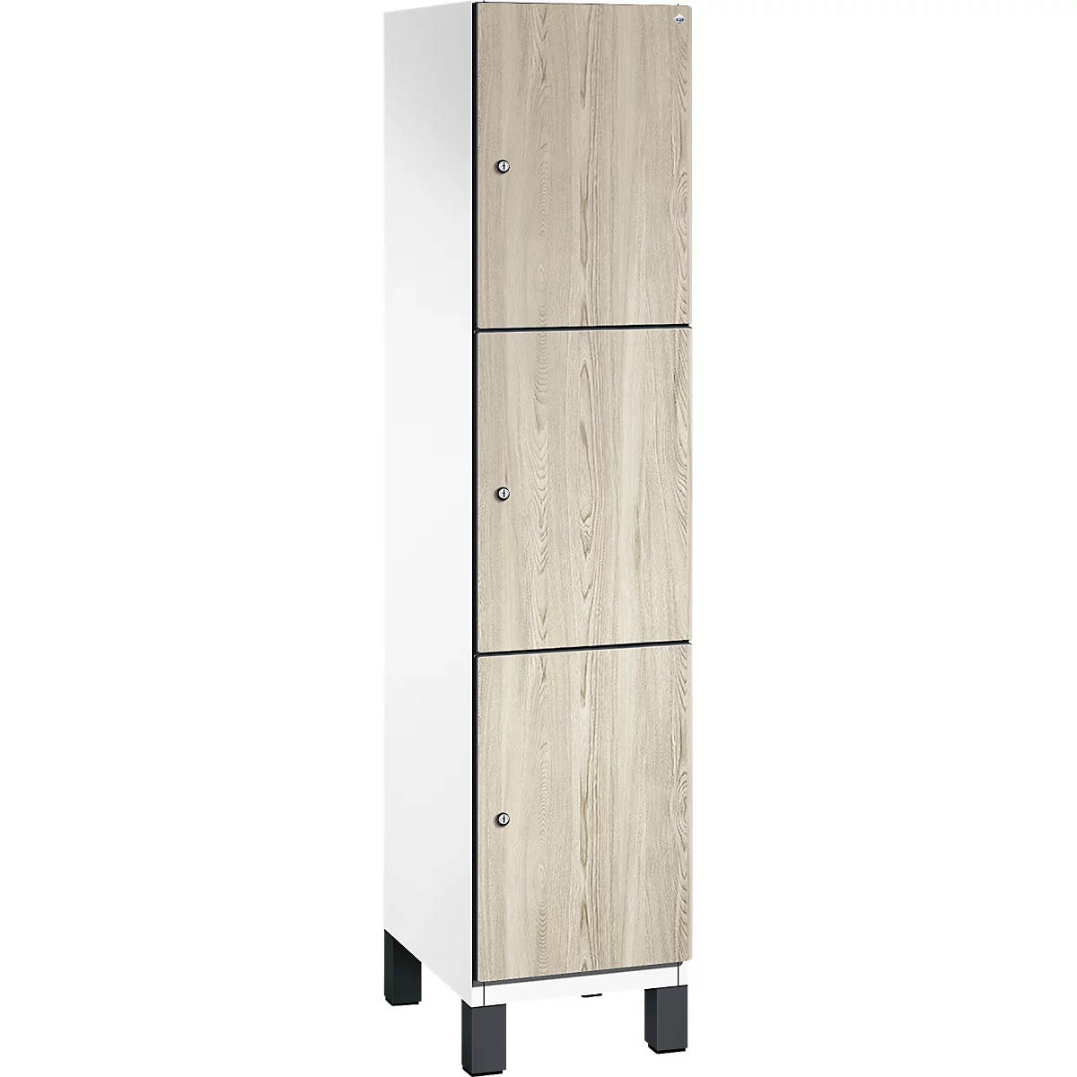 Hoher Schrank mit Holzoptikfronten. Die Türen sind dreifach unterteilt und mit silbernen Knäufen versehen. Der Schrank steht auf schwarzen Füßen.