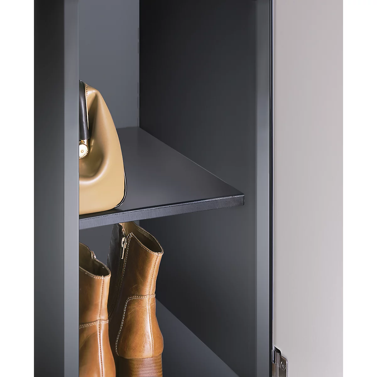 Hellbraune Handtasche und Stiefel auf dunklem Regal. Der Schrank ist offen.