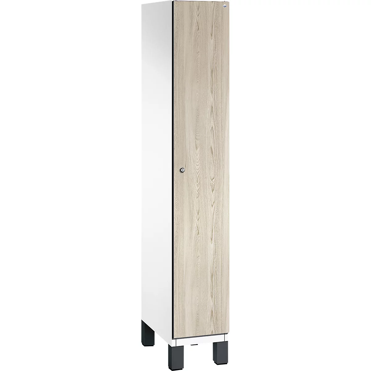 Ein weißer Schrank, mit einer Tür in Holzoptik, steht auf schwarzen Füßen.