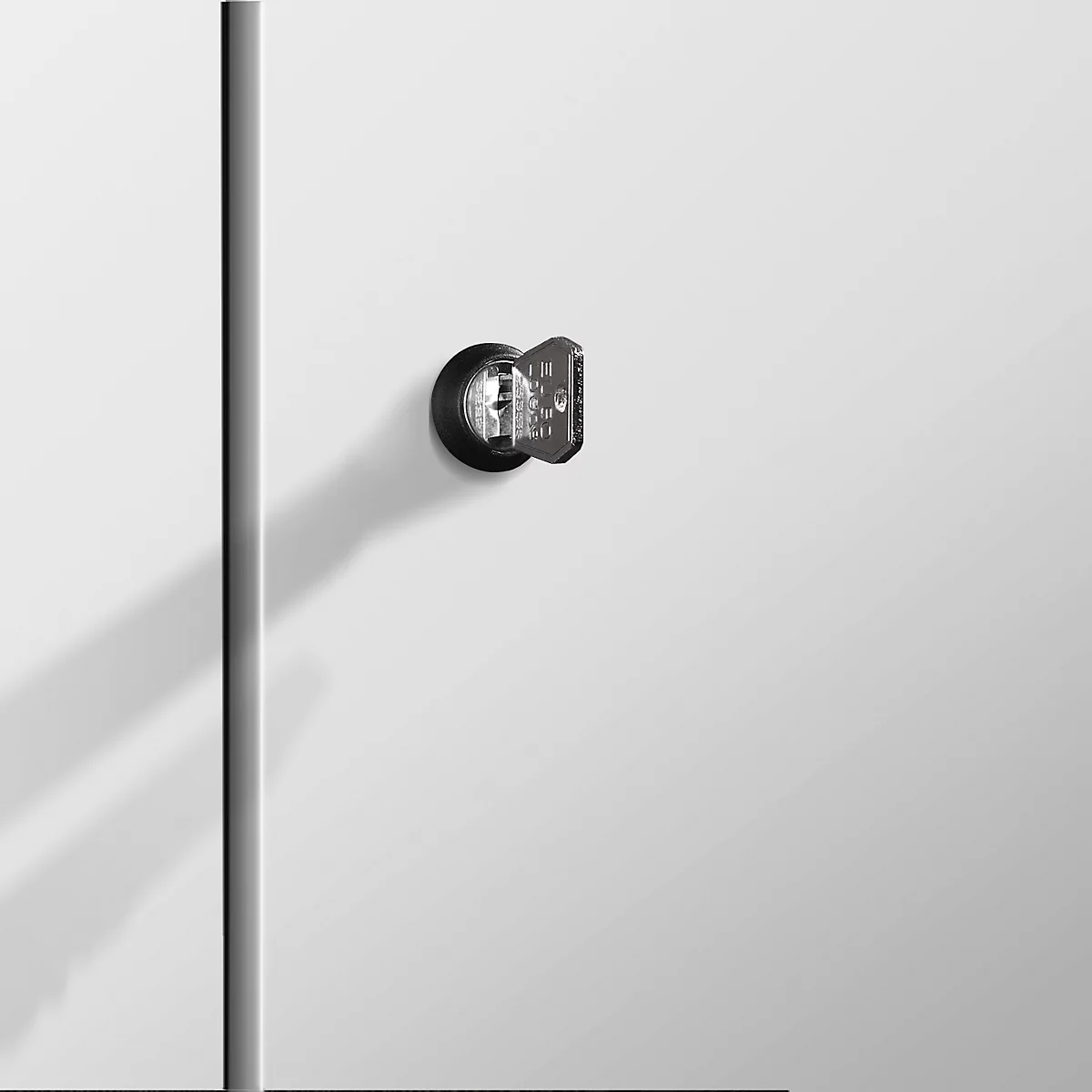 Detailaufnahme eines Türschlosses mit Schlüssel auf weißem Hintergrund. Schattenwurf rechts daneben.