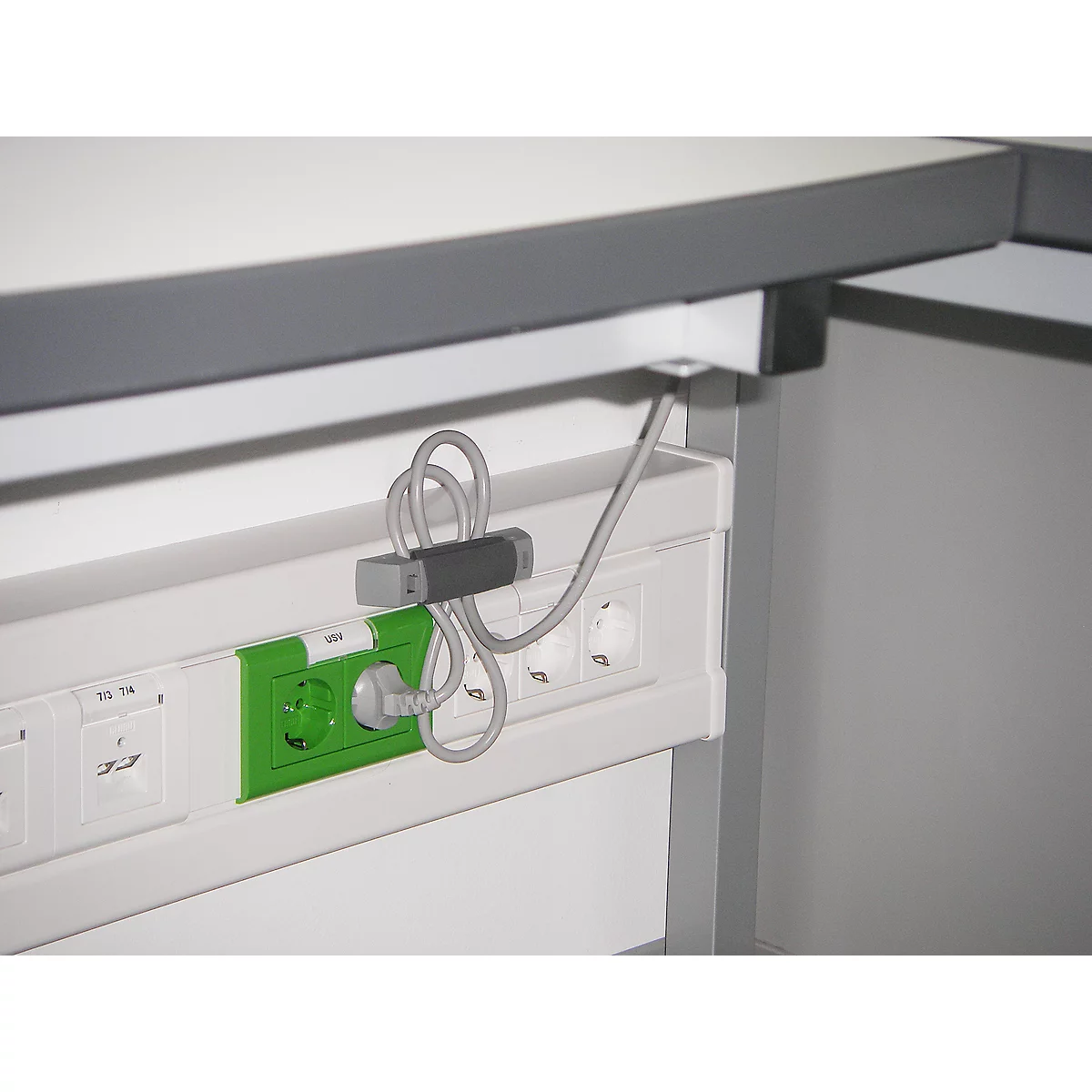 Close-up of a power strip with cable holder and plugged-in plug.