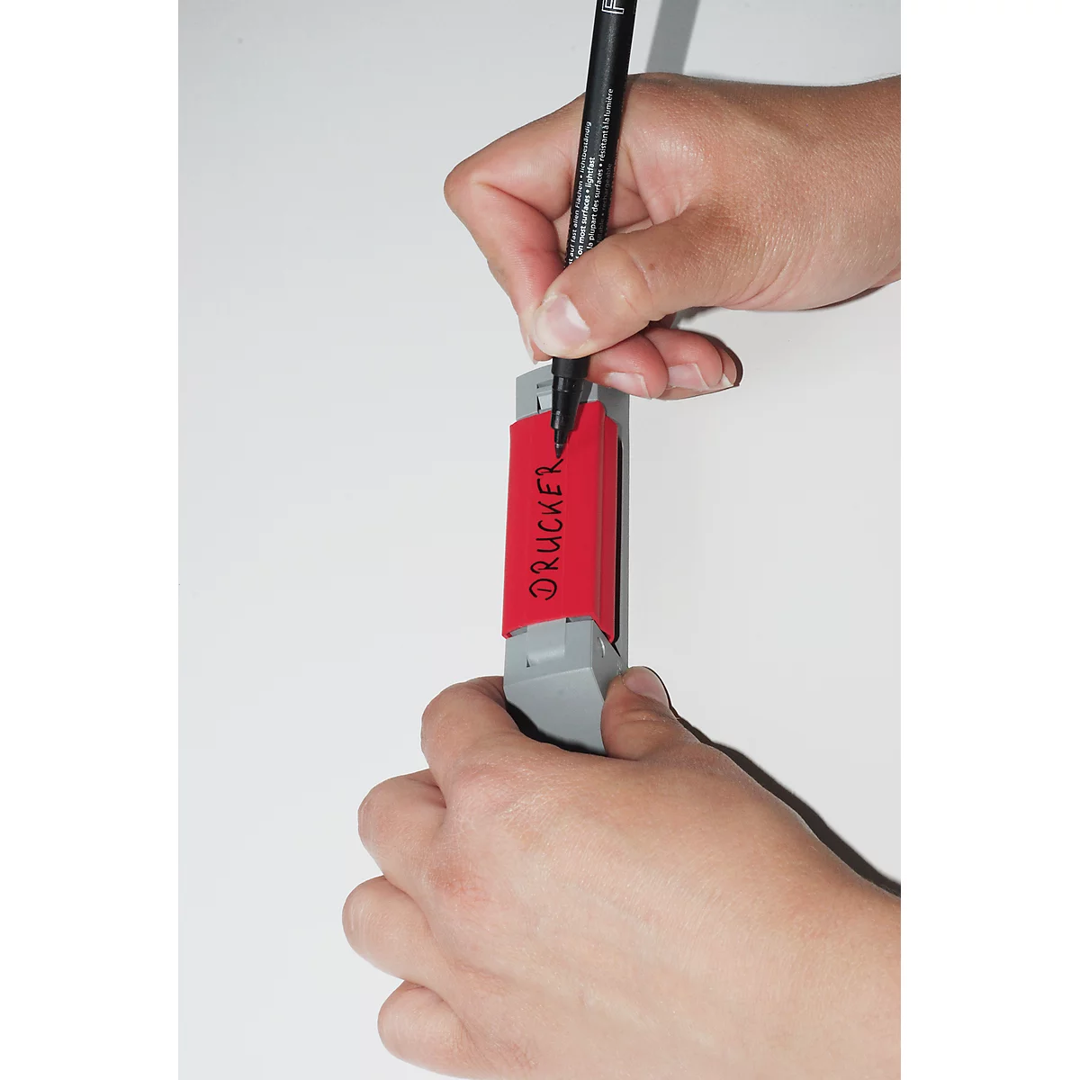 Person writing on a red sticker with a black pen. The sticker says "DRUCKER".