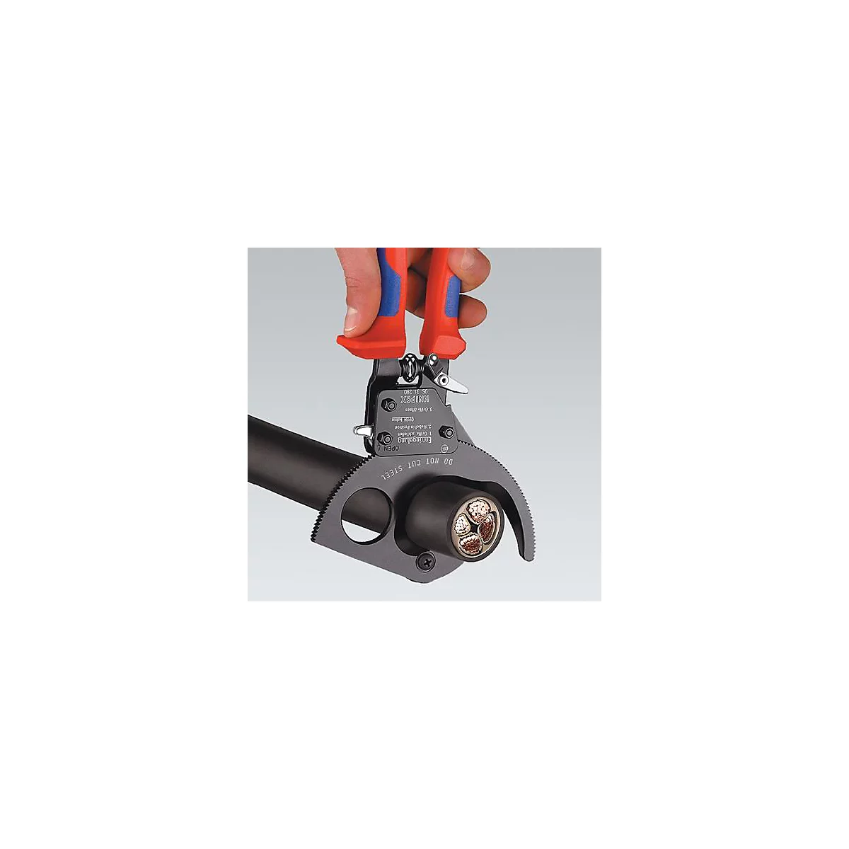 A hand holds Knipex cable stripper pliers, cutting through cable insulation and exposing the inner wires.