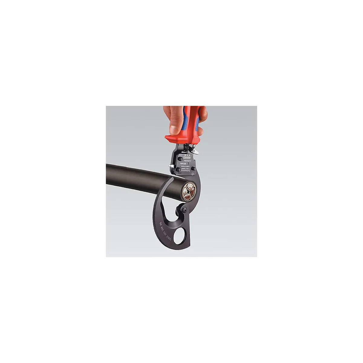 Hand holding cable cutter. The cutter surrounds a black cable, whose interior is exposed with copper conductors.