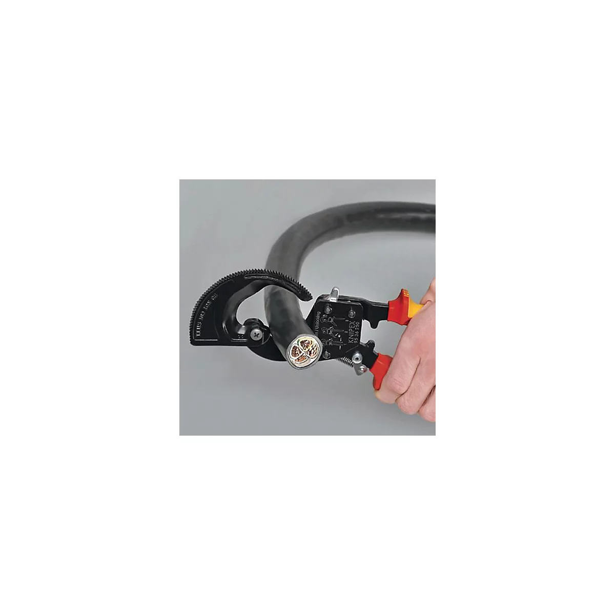 Close-up of a hand using cable cutting pliers to cut through a thick cable.